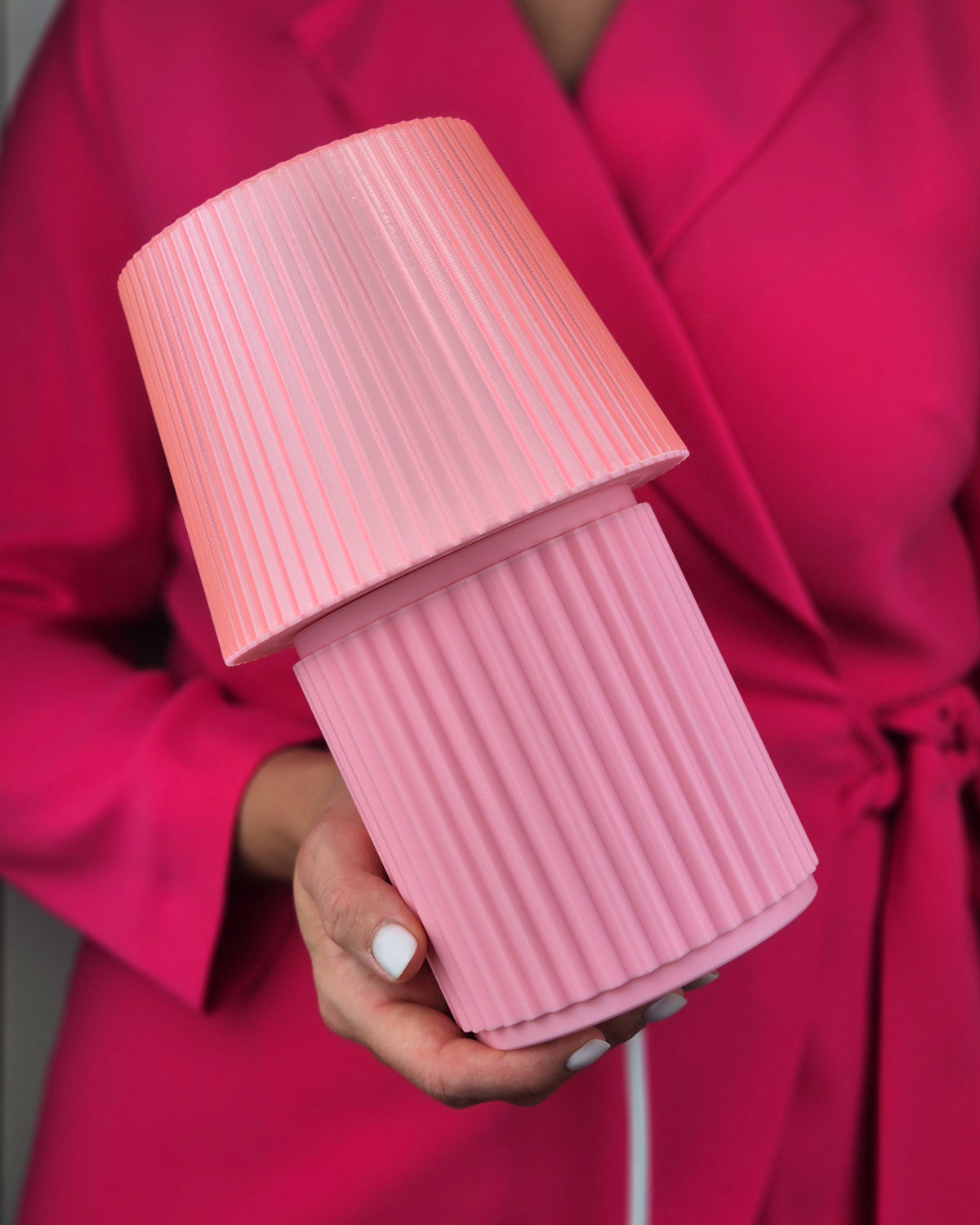 A close-up of a person in a bright pink robe holding a ribbed, two-tiered pink lamp.