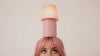 Studio video of a model with pink hair balancing the Kono Blush table lamp by Lempori on her head as the camera slowly moves in for a close-up.